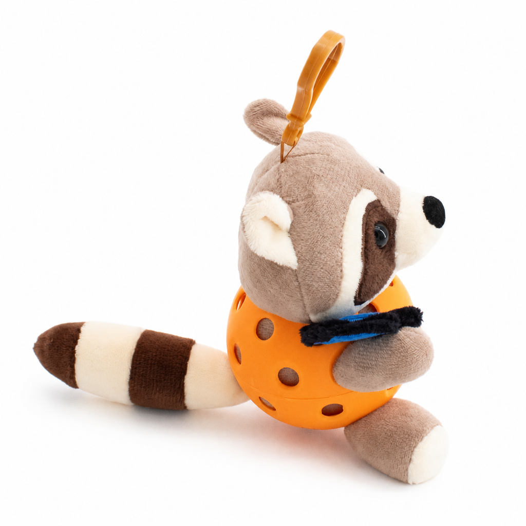 A plush raccoon toy inside an orange pickleball, attached to an orange key ring, photographed on a clean white background.