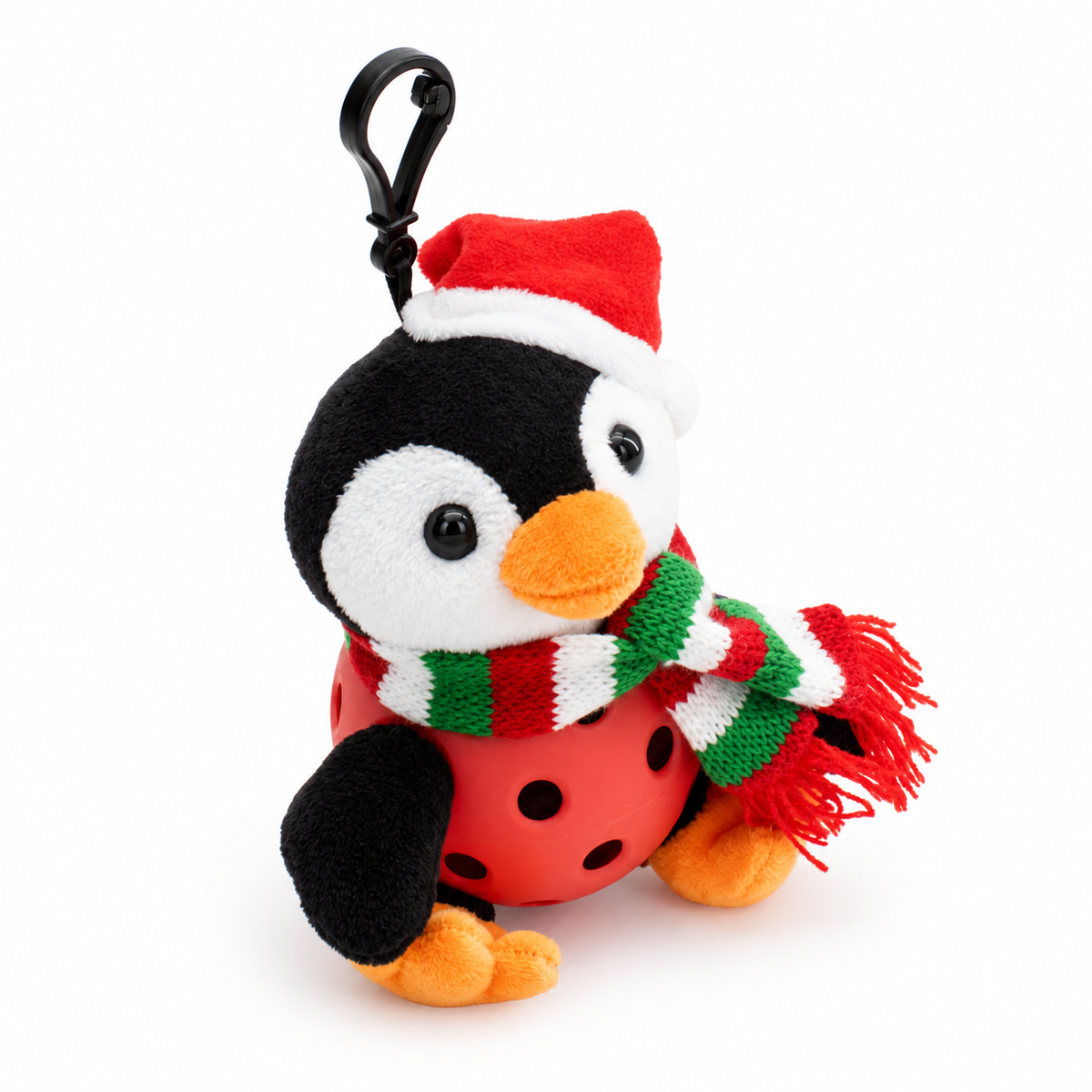 A plush penguin keychain or bag charm wearing a red Santa hat with white trim and a red, green, and white striped knit scarf, attached to a black plastic carabiner clip. The penguin is in a red pickle ball and orange feet and beak, set against a plain white background.